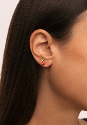 Orecchini a forma di ciliegia rossa con accento di foglia verde, realizzati in metallo. Indossati sul lobo dell'orecchio, mostrano una finitura lucida.