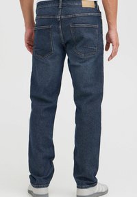Jeans in denim blu scuro con taglio dritto, design a cinque tasche e fascetta in pelle. Presentano cuciture visibili e una trama sottile.