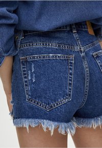 Shorts in denim blu scuro con una finitura consumata, orlo sfrangiato e design classico a cinque tasche. Cuciture visibili e dettagli in metallo.