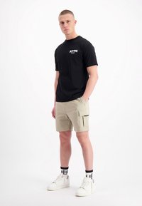 Zwarte katoenen T-shirt met een kleine graphic, in combinatie met beige cargoshorts met zijzakken en dikke witte sneakers.