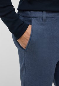 Niebieskie teksturowane spodnie o dopasowanym kroju, z bocznymi kieszeniami i wygodnym paskiem w talii, zestawione z ciemnym topem z długim rękawem.