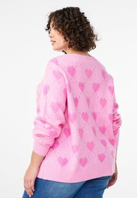 Roosa kootud kampsun tekstureeritud südamemustritega, laiade varrukate ja lõdva lõikega. Ribidega varustatud mansetid ja ääred lisavad detaile.