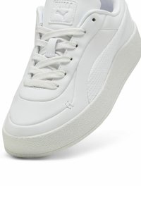 White athletic sneakers with a smooth leather upper, textured side panel, round toe, and rubber sole featuring a slightly raised edge.