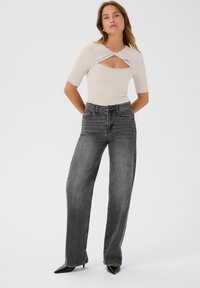 Lichtgrijze ribbeltop met een uitsnijd ontwerp, gecombineerd met zwarte hoge taille wijde jeans. Model draagt puntenlaarzen.