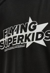 Zwarte stof met een opvallende witte grafiek met de tekst "FLYING SUPERKIDS" en een sterontwerp, waaronder staat "VAN AARHUS, DENEMARKEN."