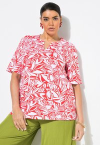 Top de patrón rojo y blanco con un corte relajado, mangas cortas y un diseño ligeramente en V. Combinado con pantalones verdes texturizados.