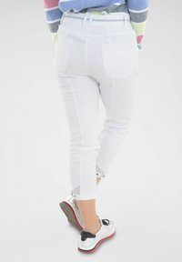 Witte cropped broeken met achterzakken, voorzien van een omslagonderrand en metalen drukknoopjes. Gecombineerd met zwarte en zilveren schoenen.
