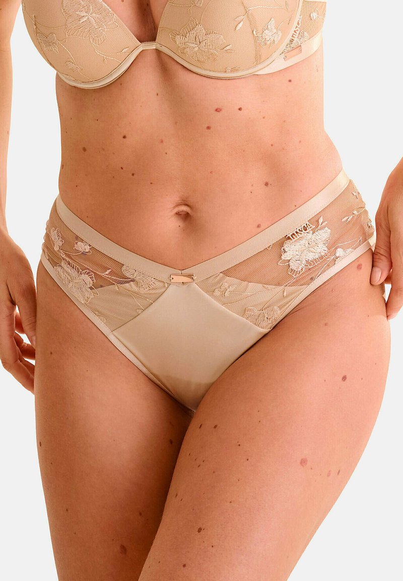 Slip in pizzo nudo con ricami floreali, presentante una parte anteriore in satin liscia e pannelli laterali in rete. Include un accento decorativo centrale in metallo.