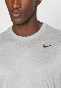 Grå bomulls t-skjorte med rund hals og korte ermer. Har en liten svart Nike-logo øverst til venstre. Myk tekstur.