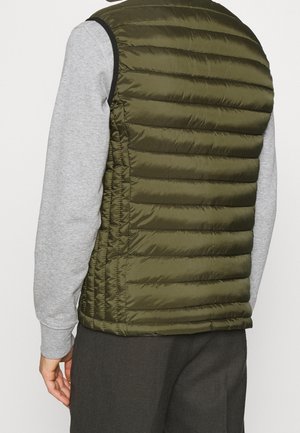 Personne portant un gilet matelassé sans manches vert olive sur une chemise gris clair à manches longues, vue de dos.