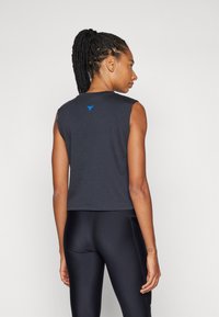 Fekete ujjatlan crop top puha anyagból, hátul kis kék logóval és kerek nyakkivágással. Fekete leggingssel párosítva.
