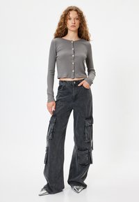 Grå ribbet langærmet crop-top med rund halsudskæring og knaplukning foran; parret med højtaljede sorte cargobukser med sidelommer.
