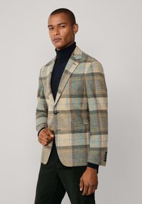 Blazer de lana de cuadros en tonos de beige, azul y marrón, con un solo botón, bolsillo en el pecho y solapas con muesca, combinado con un cuello de tortuga negro.