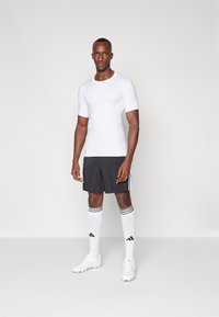 Hvitt kortermet treningsskjorte kombinert med svarte shorts. Svarte og hvite stripete sokker og hvite fotballsko fullfører den sporty stilen.