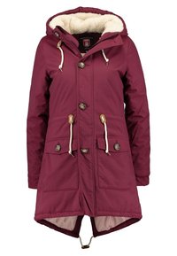 Parka color granate con capucha forrada de piel, grandes bolsillos delanteros, cintura con cordón ajustable y botones dorados. Textura suave, diseño hasta la rodilla.
