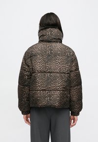 Prešita bunda z leopardjim potiskom, z visokim ovratnikom, oblazinjeno teksturo in elastičnimi manšetami, v rjavih in črnih vzorcih na svetlem ozadju.