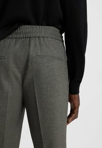 Gray tailored pants with a textured finish. Features an elastic waistband, two back pockets, and crease detailing along the front.