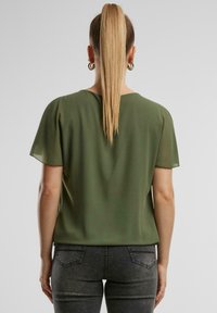 Grüne Bluse mit kurzen Ärmeln aus leichtem, glattem Stoff und einer entspannten Passform. Mit Rundhalsausschnitt und dezentem Rückendesign.