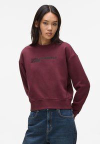 Bordeaux sweatshirt met ronde hals, geribde manchetten en zoom. Bevat het 'KARL LAGERFELD JEANS' logo in het zwart op de borst. Gecombineerd met blauwe jeans.