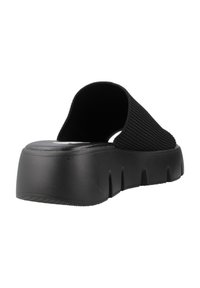 Zapato negro tipo slip-on con parte superior de tela acanalada, suela de plataforma de goma gruesa con ranuras horizontales y un diseño minimalista.