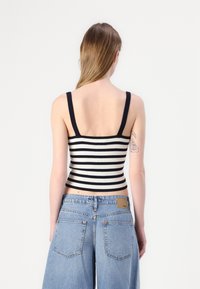 Černobíle pruhovaný žebrovaný crop top s širokými ramínky, přiléhavý střih a texturovaný povrch, spárovan�ý se světle modrými džínami s vysokým pasem.
