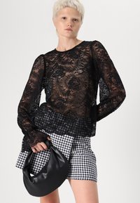 Black lace long-sleeve top with floral patterns, paired with a checkered black-and-white skirt. The model holds a black, sleek handbag.