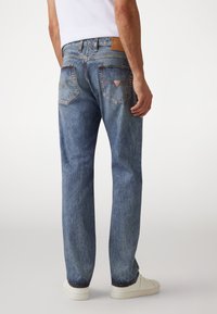 Vervagende blauwe denim jeans met een rechte pijpdesign, een gelabelde leren patch op de tailleband, en opvallende accenten op de achterzak.