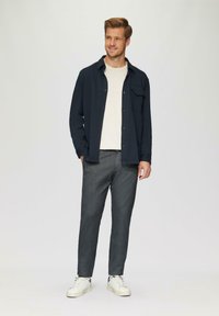 Marineblauw overhemd met knopen over een lichtbeige ronde hals, gecombineerd met grijze, gestructureerde broek en witte sneakers. Eenvoudig, aansluitend ontwerp.