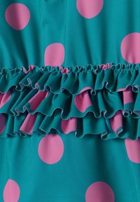 Tissu teal avec de grands pois roses, featuring un accent froncé rose à la taille. La texture semble lisse avec un léger éclat.