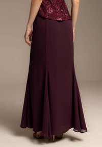 Falda larga burdeos de tela fluida, con un diseño acampanado y una abertura modesta, complementada con una blusa de patrón texturizado.