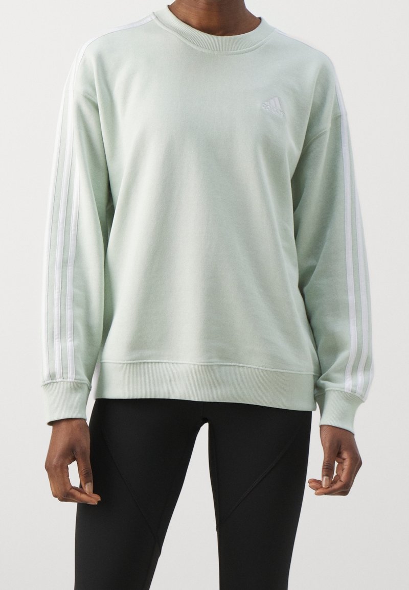 Light green sweatshirt with long sleeves, white stripe accents, ribbed cuffs, and crew neckline. Features subtle logo on chest. Black leggings visible.