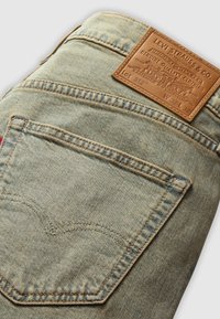 Jean en denim bleu clair plié pour montrer la poche arrière et l’étiquette en cuir marron Levi Strauss avec les détails de la marque et de la taille.