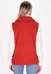 Rote Fleeceweste mit strukturiertem Finish, hohem Kragen und weißen Strickärmeln. Mit roten Akzentknöpfen an der Taille.