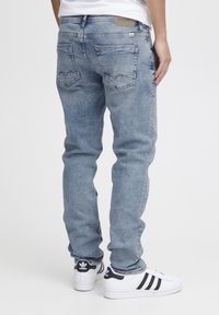 Vaqueros de denim azul claro con un corte slim, que presentan bolsillos traseros con costura en zigzag y un parche de cuero con marca en la cintura.