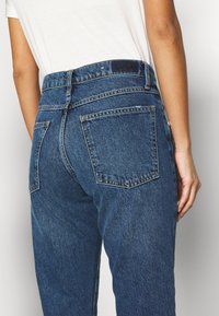 Blå denimjeans med hög midja, med två bakfickor och synliga sömmar. Tyget har en texturerad, något blekt finish.