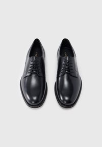 Paire de chaussures habillées noires en cuir poli à lacets sur un fond gris clair, vues de dessus.