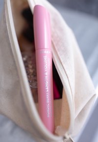 Pink mascara tube mærket "Nordic Berry Length & Volume" inde i en beige canvas makeup pouch, der afslører sin cylindrisk form og glatte tekstur.