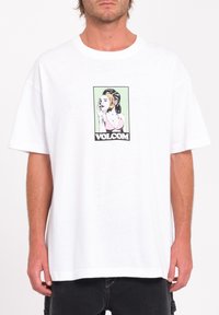 T-shirt en coton blanc avec un imprimé graphique d'une femme en bikini rose, entourée d'un fond vert, et le texte "VOLCOM" en bas.