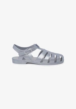Gray plastic sandal with open design, multiple slits on the upper, ankle strap with adjustable buckle, and flat sole.