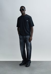 Μαύρο κοντομάνικο μπλουζάκι με τσέπη στο στήθος, σε συνδυασμό με σκουρόχρωμο, ταλαιπωρημένο τζιν. Το μοντέλο φοράει υπερμεγέθη μαύρα γυαλιά ηλίου και μαύρα παπούτσια.