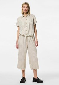 Jumpsuit a righe beige con maniche corte, chiusura frontale a bottoni, cintura annodata in vita e gambe larghe e cropped. Abbinato a mocassini neri.