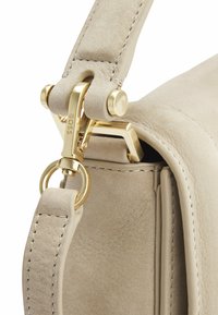 Beige mockakskinnväska med ett clasp i guldmetall och ringfäste. Har en slät kant och synliga stygn på axelremmen.