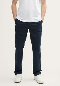 Pantalones azul marino, diseño de pierna recta, hechos de tela ligera. Cuenta con bolsillos laterales y pasadores para cinturón, combinados con zapatillas blancas.