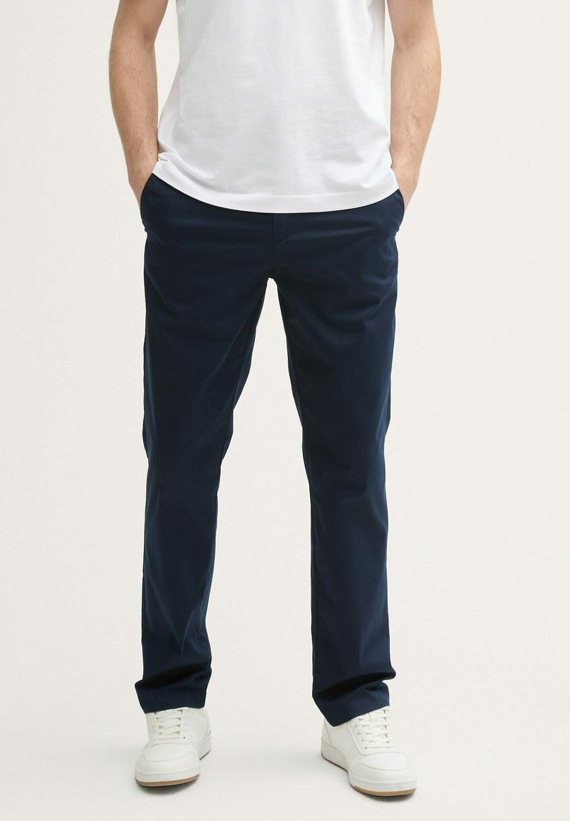 Pantalones azul marino, diseño de pierna recta, hechos de tela ligera. Cuenta con bolsillos laterales y pasadores para cinturón, combinados con zapatillas blancas.