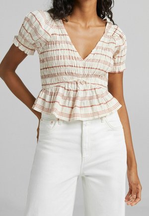 Witte top met rode horizontale strepen, gerimpelde borst, korte pofmouwen en een peplumzoom, gecombineerd met witte high-waisted jeans.