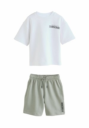 Tricou alb cu mânecă scurtă, cu inscripția "SUBSCRIBE" în negru; combinat cu pantaloni scurți verzi deschis având o imprimeu similar și un curea elastică.