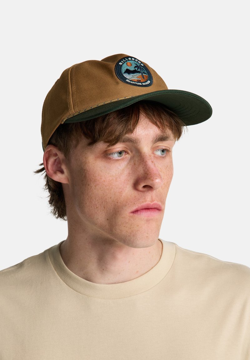 Καφέ καπέλο με πράσινη γείσο, με κεντημένο έμβλημα στο μπροστινό μέρος που απεικονίζει βουνά και ήλιο. Ομαλή υφή υφάσματος.