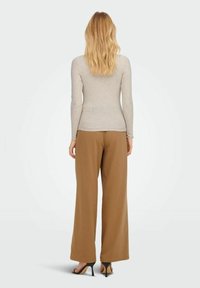 Tailliertes langärmliges Rippoberteil in hellbeige, kombiniert mit lockeren braunen Hosen. Das Outfit zeichnet sich durch eine glatte Textur und neutrale Farben aus.
