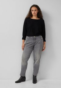Haut noir à manches longues, jean gris droit légèrement délavé et bottines noires. Design simple et coupe décontractée. Pas de motifs notables.