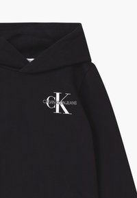 Černá mikina s kapucí s vyšitým logem Calvin Klein Jeans v bílé a šedé barvě na levé hrudi, s sklopenou kapucí.